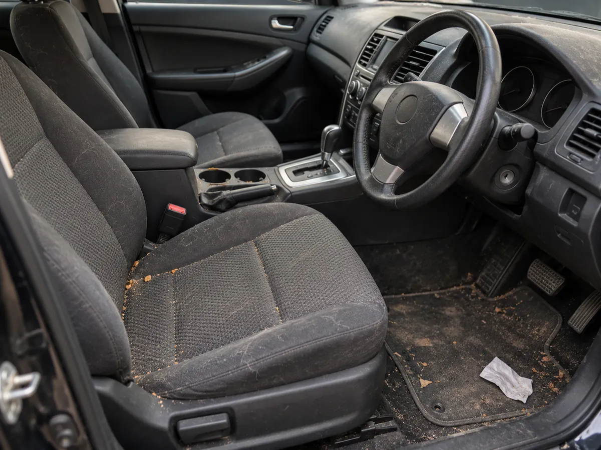 Dirty car interior before detailing, with crumbs and dirt on the seats and floor